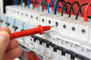 Hand of an electrician inspecting a circuit breaker & panel