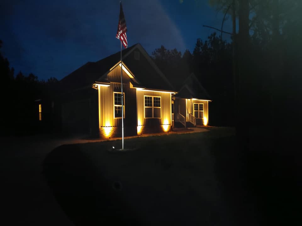 Landscape lighting in front of an updated home at night with a flag pole in front yard.